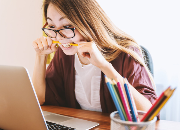 a student nervously biting her pencil and typing on her laptop.